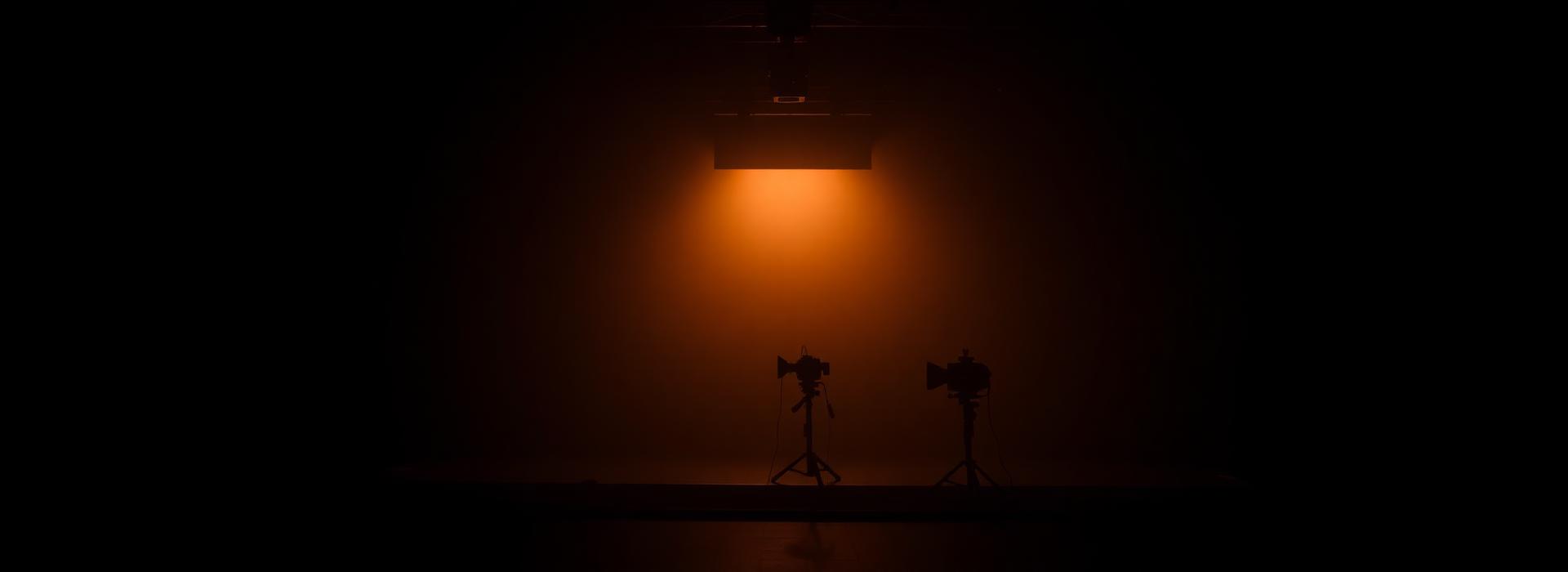Dark soundstage with a single warm key light and camera silhouettes